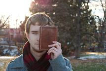 college student holding a Bible in front of half his face