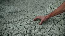 Hand touches dry soil with cracks