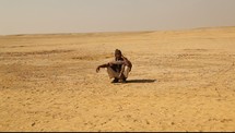a man squatting in the desert 