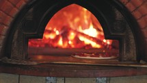 Italian pizza is cooked in a wood-fired oven. Pizza oven in restaurant. Tasty pizza getting from oven.