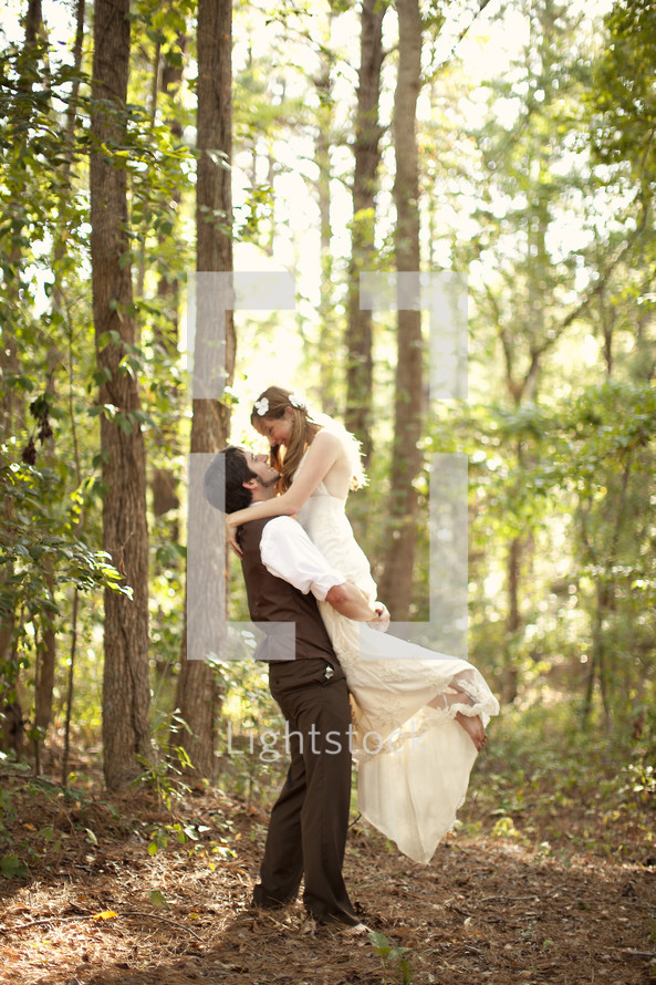 Groom holding bride in arms outdoors