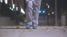 feet of a man walking down a sidewalk alone at night 