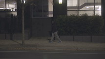 a young man walking alone on a sidewalk at night 