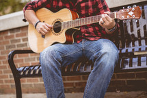 man sitting on a bench playing a guitar 