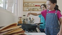 Two young girls preparing pancakes in the kitchen using a frying pan