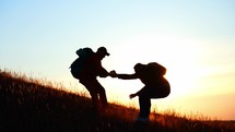 Silhouette two people working in team mountain rock climbing. Helping hand friend to overcome difficulties. Dangerous sport in nature. Business partner. Tourists with backpack and hiking accessories.