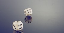 Slow motion macro shot of white dice falling and rolling on reflective surface