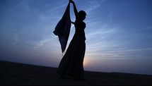 woman with a scarf dancing in a desert at sunset 
