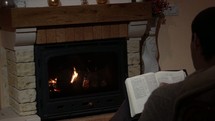 a man reading a Bible in front of a fireplace 