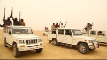 men with rifles riding in trucks through a desert