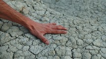 Hand touches dry soil with cracks