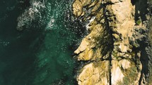 aerial view over waves along a rocky shore 