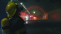 Firefighters inside a dark tunnel with emergency lights in the background