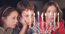 Three young kids watching Hanukkah candles burning.