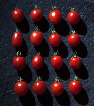 cherry tomatoes on black background arranged in a linear way.