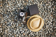 straw hat, camera, and canteen on gravel