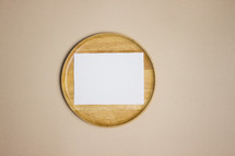 Blank white note on wooden plate on tan background