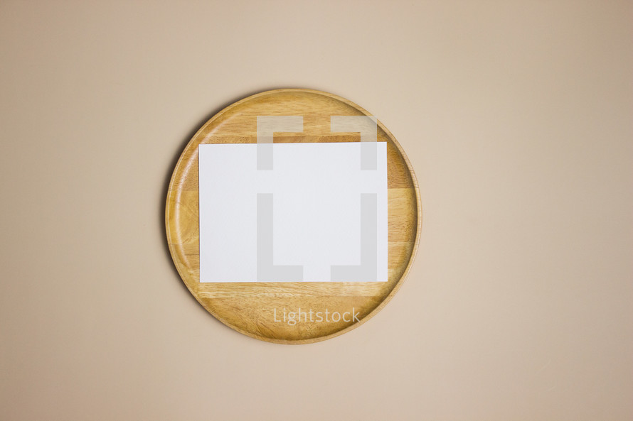 Blank white note on wooden plate on tan background