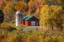 Silo and red and green barn surrounded by trees with autumn foliage