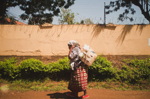 woman walking on a dirt road carrying bags