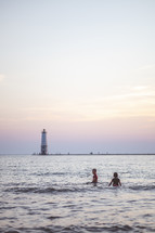kids playing in the ocean with view of a Lighthouse 
