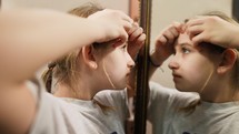 Young teenager girl squeezing acnes on skin face front mirror. Portrait of a teenager with problem skin. Girl teenager squeezes pimples on her face. Youth skin care.