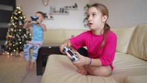 Video game concept. Pretty girl and little boy playing game console and laughing while sitting on sofa at home. Girl playing video games with a joystick. Child gambling addiction.