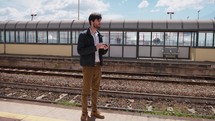 Young Man Uses The Phone While Waiting For The Train At The Station