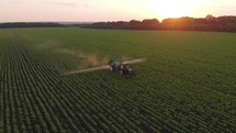 Aerial view of farming tractor spraying on field with sprayer, herbicides and pesticides at sunset. Farm machinery spraying insecticide to the green field, agricultural natural seasonal spring works.
