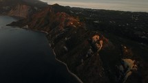 Flying above the mountains on an island surrounded by the ocean during sunset