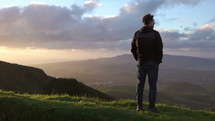 man standing on a mountaintop looking out at a sunrise 