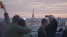 Unrecognizable Tourists on the rooftop of Galeries Lafayette Haussmann enjoying the sunset with the iconic Eiffel Tower and the city buildings of Paris in the background