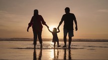 Happy Modern Southeast Asian Indonesian Family Enjoying Sunset Together on The Beach. Silhouette of Father Mother and Child in Slow Motion.