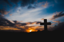 silhouette of a hand holding up a small cross at sunset 