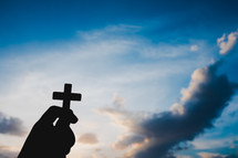 silhouette of a hand holding up a small cross 
