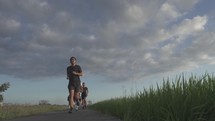 Three healthy active Asian Indonesian Men Running in Slow Motion on Beautiful Outdoor Nature Green Grass Rice Field Jogging Track During Sunset - Bali Indonesia