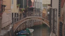 The atmosphere of narrow canals in the city of Venice, with many bridges and small boats parked.