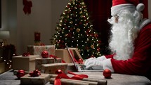 Santa Claus writing on Pc under Christmas tree 