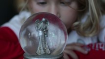 girl child staring at an angel snow globe 