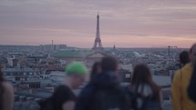 Unrecognizable Tourists on the rooftop of Galeries Lafayette Haussmann enjoying the sunset with the iconic Eiffel Tower and the city buildings of Paris in the background