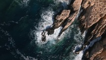Power of the ocean, waves crashing on a rocky coastline, aerial top down drone view