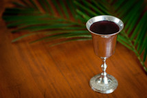 silver goblet of wine on a table with a palm leaf