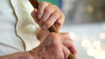 Elderly mans wrinkled hands resting on his cane