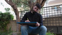 Young Man Writes On A Blackboard While Sitting Under A Tree