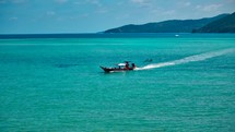 Wooden boat in turquoise sea, movement on blue water. Trip boat with tourists sailing on clean blue sea surface. A long-tailed Thai boat sails among the islands, touristic excursion ride. Aerial. 