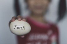 girl holding an Easter egg stamped with the word faith 
