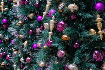 Purple and gold ball Christmas ornaments hanging from pine Christmas tree.