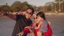 Happy Modern Southeast Asian Indonesian Family Enjoying Sunset Together on The Beach. Silhouette of Father Mother and Child in Slow Motion.