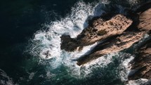 Waves crashing on a rocky beach during sunset, top down aerial drone view