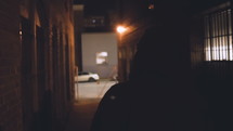 a man in a hoodie walking down an alley at night 